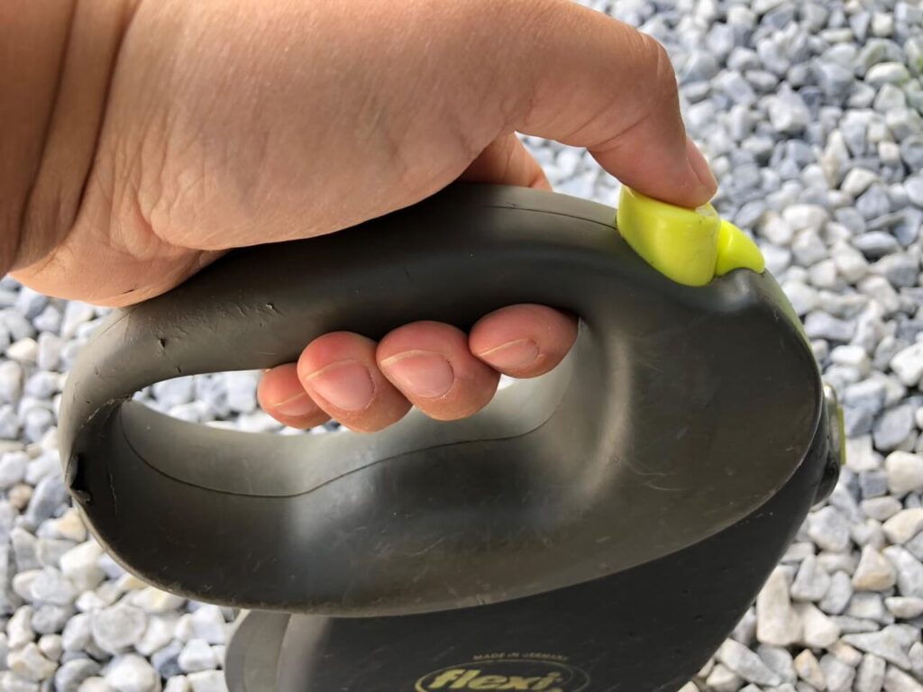 Blick von der Seite auf eine Flexileine mit dem Daumen auf der Bremse