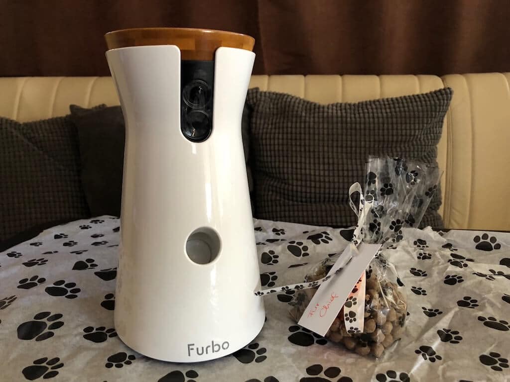 Die Hundekamera Furbo auf einem Tisch daneben ein Päckchen Leckerlies