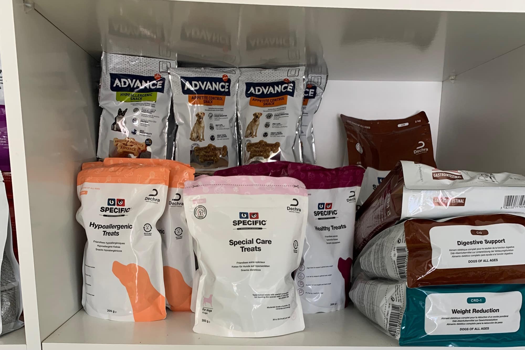 Bei einer Verschiedene Trockenfutterbeutel und Leckerchenpackungen in einem Regal. Beschriftung lautet: Bei einer Futtermittelallergie von deinem Hund brauchst spezielles Futter.